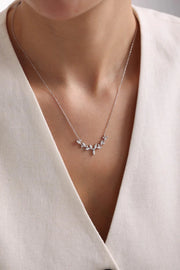 A woman wearing a delicate silver chain necklace with a curved centerpiece designed as a vine with sparkling, marquise-cut crystal leaves.