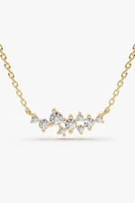 A delicate gold chain necklace with a curved horizontal bar of sparkling, round-cut clear gemstones in various sizes, set against a plain white background.