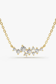 A delicate gold chain necklace with a curved horizontal bar of sparkling, round-cut clear gemstones in various sizes, set against a plain white background.
