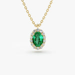 A close-up of a gold chain necklace with an oval-cut emerald green gemstone pendant, which is surrounded by a halo of small, round-cut clear gemstones.