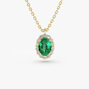 A close-up of a gold chain necklace with an oval-cut emerald green gemstone pendant, which is surrounded by a halo of small, round-cut clear gemstones.