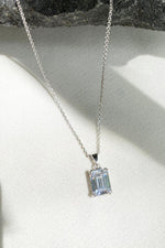 A delicate silver chain necklace featuring a rectangular, emerald-cut clear gemstone pendant.


