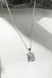 A delicate silver chain necklace featuring a rectangular, emerald-cut clear gemstone pendant.


