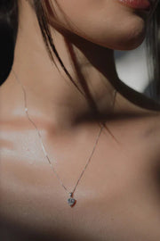 A woman wearing a delicate silver box chain necklace with a brilliant, heart-shaped clear crystal pendant.
