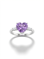 A woman's hand wearing a silver ring featuring a large, heart-shaped lavender gemstone center flanked by two small clear baguette stones.