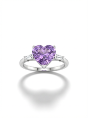 A woman's hand wearing a silver ring featuring a large, heart-shaped lavender gemstone center flanked by two small clear baguette stones.