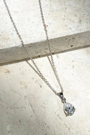 A delicate silver chain necklace with a brilliant, teardrop-shaped clear crystal pendant.

